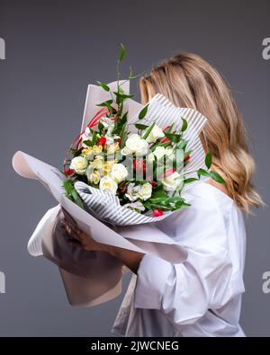 Donna in camicia bianca contiene un bouquet di fiori con rose, tulipani e verde. Foto Stock