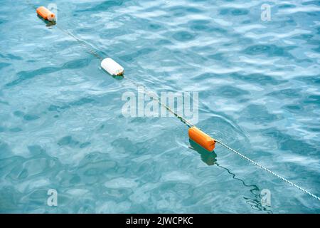 Installate boe luminose rosse e bianche che ondulano sulla superficie dell'acqua blu. Boe attrezzate mostrano bordo di acqua consentito per il turista sicuro nuoto closeup Foto Stock