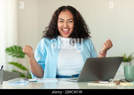 Black Lady che usa il notebook gesturing Sì festeggia il successo sul posto di lavoro Foto Stock