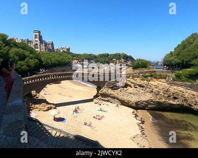 Biarritz, Pirenei Atlantici. Francia: 11 luglio 2022: Vista del famoso ponte di pietra per il Rocher du Basta, paesaggio urbano e costa con bache di sabbia Foto Stock