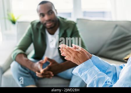 Uomo nero pensivo seduto sul divano presso il gabinetto psicoterapeuta e ascoltando lo specialista, concentrarsi sulle mani dello psicologo Foto Stock