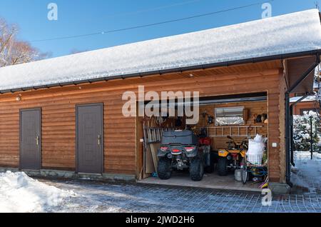 Vista sulla facciata porta aperta ATV casa garage con quad fuoristrada veicolo parcheggiato sole neve fredda giornata invernale. ATV avventura sport estremo. Casa organizzata Foto Stock