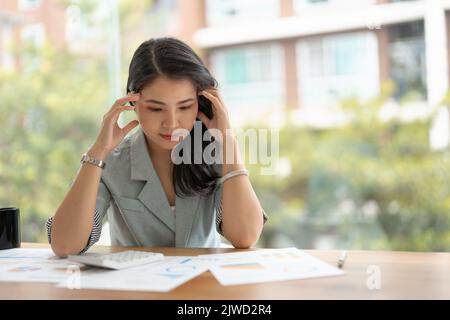 Donna asiatica pensierosa che gestisce il budget e le finanze utilizzando la calcolatrice in ufficio, il concetto di contabilità finanziaria. Foto Stock