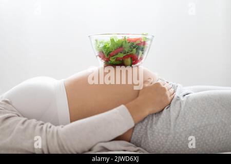 Ciotola con insalata fresca sul ventre di donna incinta Foto Stock