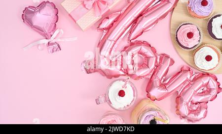 Tavolo dolce con ballon e deliziose torte da tazza con crema e spazio copia su tema rosa pastello. Giacitura piatta Foto Stock
