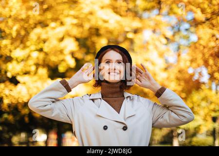 Sorridente rossa bella giovane donna europea in impermeabile e cappello godere del bel tempo, tempo libero Foto Stock