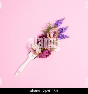 Pennello creativo con fiori primaverili su sfondo rosa pastello. Giacitura piatta Foto Stock