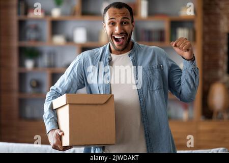 Concetto di consegna. Excited Black Man Holding scatola di cartone grande a casa Foto Stock