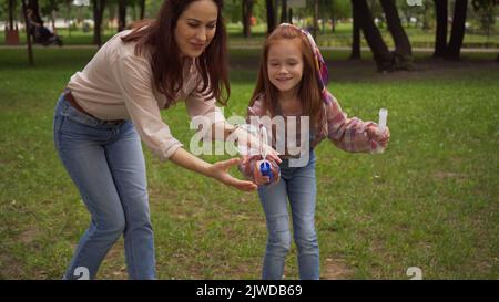 Sorridente genitore e ragazza che tiene bolle di sapone nel parco estivo, immagine stock Foto Stock