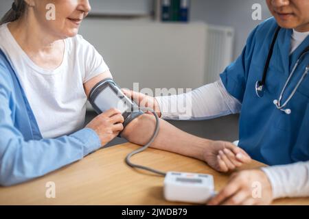 Il medico asiatico di sesso maschile adulto concentrato misura la pressione con tonometro per la paziente anziana in clinica Foto Stock