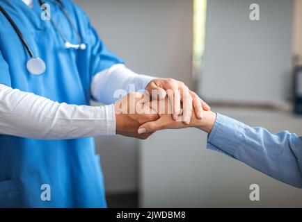 Medico maschile giovane in uniforme calmante, scuotendo la mano con la vecchia paziente in clinica Foto Stock