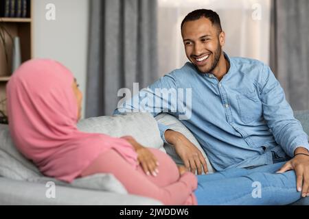 Felice incinta sposi musulmani neri che chiacchierano e si rilassano a casa Foto Stock
