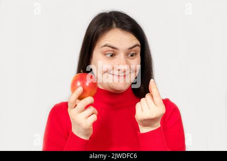 Una donna in rosso tiene una mela e una pillola nelle sue mani. Vitamine in forma naturale e in integratori alimentari sintetici Foto Stock