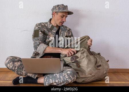 Soldato occupato con zaino utilizzando un portatile militare Foto Stock