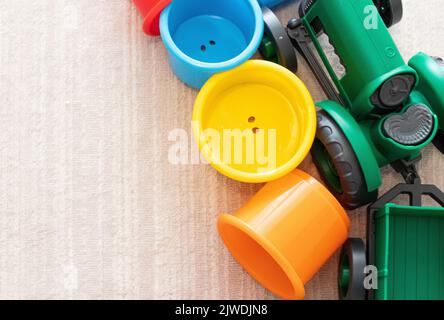 Sfondo dei giocattoli per bambini o bambini. Vista dall'alto dei giocattoli colorati. Trattore verde e coppe in plastica di diversi colori. Foto rumorosa e orizzontale. Nessuna gente. Foto Stock