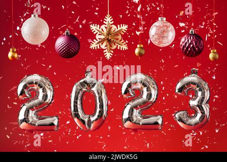 2023 Celebrazione di Capodanno - numeri di palloncino e decorazioni su sfondo rosso brillante glitter Foto Stock