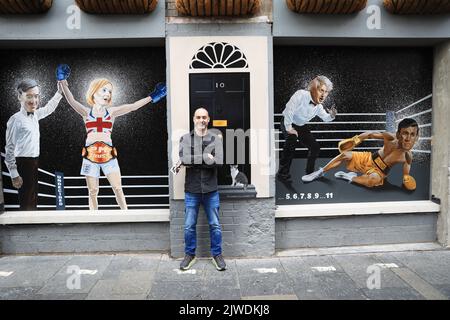 L'artista Ciaran Gallagher accanto al suo nuovo murale raffigurante Liz Truss che è stato dichiarato vincitore da Jacob Rees Mogg dopo aver battuto Rishi Sunak, che è contato da Boris Johnson, in una partita di boxe, Che è stata svelata a Belfast dopo che la signora Truss ha vinto le elezioni di leadership del partito conservatore, diventando il prossimo primo ministro. Data immagine: Lunedì 5 settembre 2022. Foto Stock