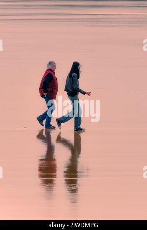 Luce serale sui turisti che camminano sulla spiaggia di Fistral a bassa marea a Newquay in Cornovaglia. Foto Stock