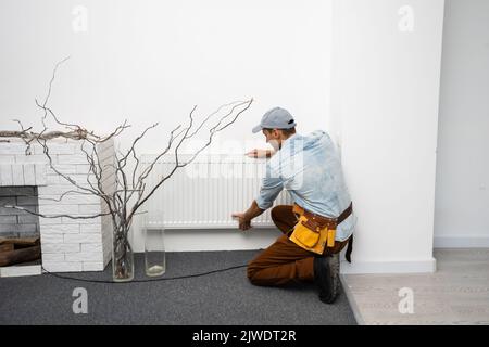 Un uomo cambia il riscaldamento in casa, radiatori. Il concetto di riscaldamento moderno, sostituzione del vecchio con uno nuovo. Calore in casa Foto Stock