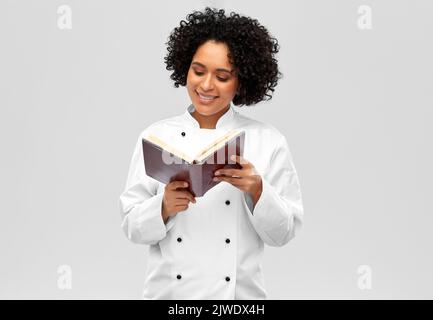 sorridente cuoco femmina che legge il libro del cuoco Foto Stock