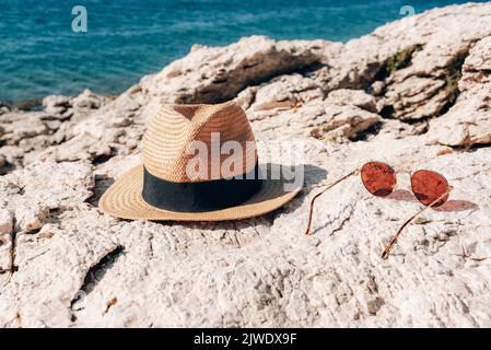 Cappello di paglia e occhiali da sole sulla costa rocciosa. Concetto di vacanza estiva Foto Stock