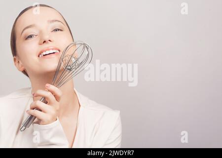 Lo chef tiene una frusta e si posa con lui su sfondo bianco. Scuola di cucina Foto Stock