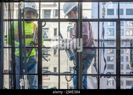 Operai edili fuori da una finestra sopra una strada urbana a New York City in un paniere sospeso, Midtown Manhattan, USA 2022 Foto Stock