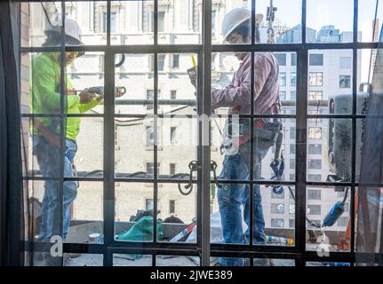 Operai edili fuori da una finestra sopra una strada urbana a New York City in un paniere sospeso, Midtown Manhattan, USA 2022 Foto Stock