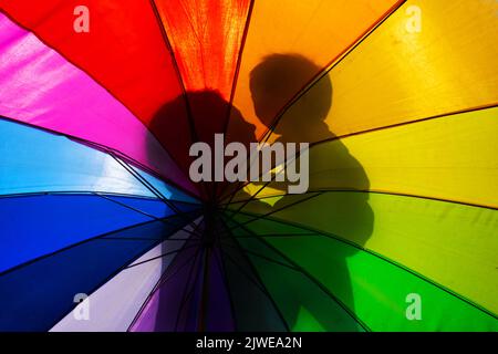 Silhouette di una madre che tiene un bambino attraverso un ombrello multicolore Foto Stock