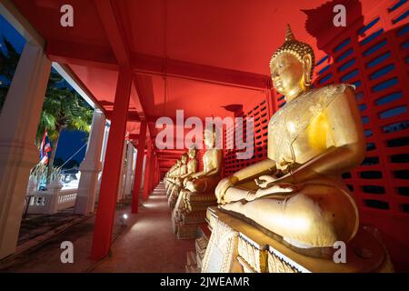 Diverse statue dorate di statue di Buddha in posizione meditativa sono allineate in un corridoio e punteggiano su ogni statua di fronte alla parete rossa. Foto Stock