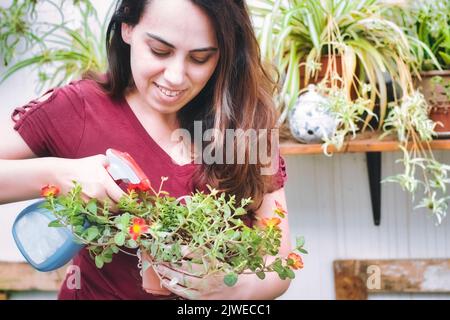 Una giovane donna che si prende cura del suo giardino, spruzzando acqua sulle piante di casa in pentole a casa nel suo capannone Foto Stock