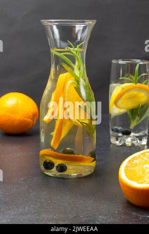 Bevanda estiva infusa con arance, mirtilli e rosmarino in bottiglia. Arancione sul tavolo. Sfondo nero Foto Stock