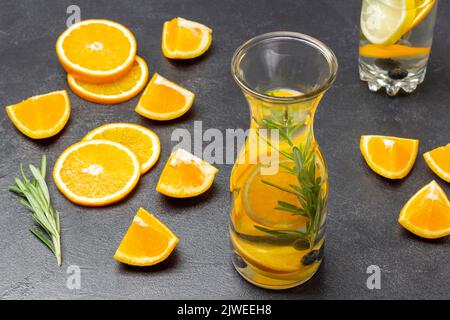 Bevanda estiva infusa con arance, mirtilli e rosmarino in bottiglia. Fette di arancia tagliate e rametto di rosmarino sul tavolo. Sfondo nero Foto Stock