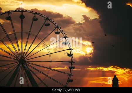 Ruota panoramica nel parco divertimenti e nuvole sceniche al tramonto in cielo e silhouette di uccelli volanti Foto Stock