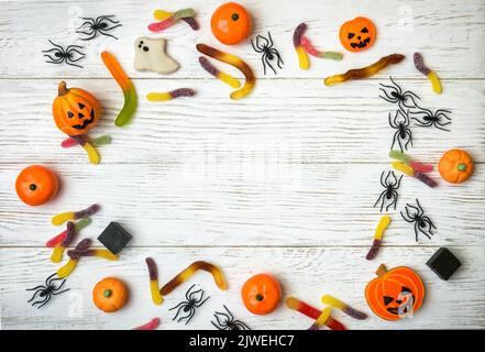 Dolci di Halloween e decorazioni su sfondo di legno bianco. Vista dall'alto della cornice di Halloween con biscotti, fantasma, ragni e caramelle su un tavolo di legno, piatto la Foto Stock