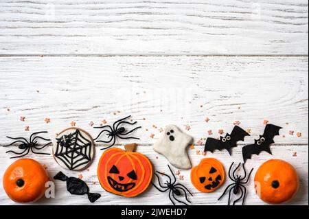 Dolci di Halloween e decorazioni su sfondo di legno bianco. Vista dall'alto della cornice di Halloween con biscotti, fantasma, ragni e pipistrelli su un tavolo di legno, piatto Foto Stock