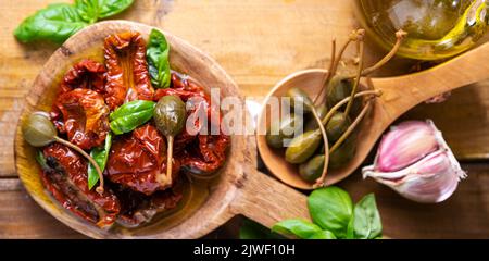 Capperi e pomodori secchi con erbe in olio di oliva. Capperi grandi. Antipasti tradizionali in Italia con aglio, erbe provenzali e basilico. Ingredienti per bruschetta e aperitivo. Vista dall'alto Foto Stock