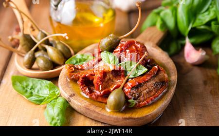 Capperi e pomodori secchi con erbe in olio di oliva. Capperi grandi. Antipasti tradizionali in Italia con aglio, erbe provenzali e basilico. Ingredienti per bruschetta e aperitivo. Foto di alta qualità Foto Stock