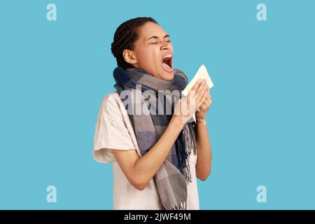 Donna malata con greggi neri si sente male, starnuti nei tessuti, soffre di naso che corre, sintomi freddi o allergia, indossando una camicia bianca. Studio in interni isolato su sfondo blu. Foto Stock