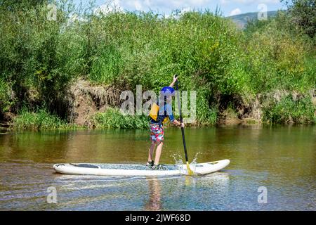 Stand up paddle boarding ragazzo, Roaring Fork River, vicino Aspen, Colorado USA Foto Stock