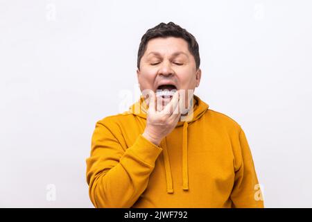 Uomo di mezza età che mette un piatto morso in bocca per proteggere i suoi denti di notte da macinazione causata dal bruxismo, indossando felpa con cappuccio in stile urbano. Studio in interni isolato su sfondo bianco. Foto Stock