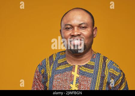 Ritratto di giovane africano in costume nazionale sorridente alla macchina fotografica isolata su sfondo giallo Foto Stock