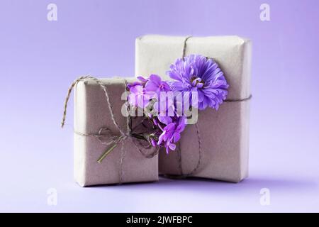 Due scatole regalo in carta artigianale grigia decorate con fiori di lilla in castoro su sfondo viola per le vacanze, vista frontale Foto Stock