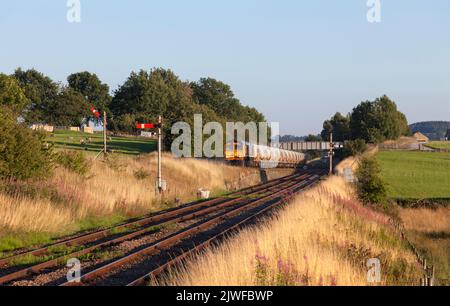 GB Rail Freight Classe 66 Locomotiva diesel 66754 che passa i segnali ferroviari del semaforo a Settle Junction con un treno merci che trasporta cemento Foto Stock