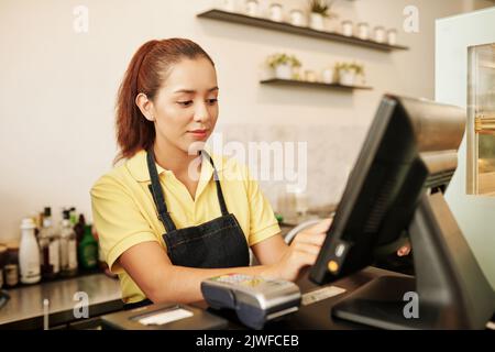 Cameriera sorridente al cafè che lavora al banco della cassa Foto Stock