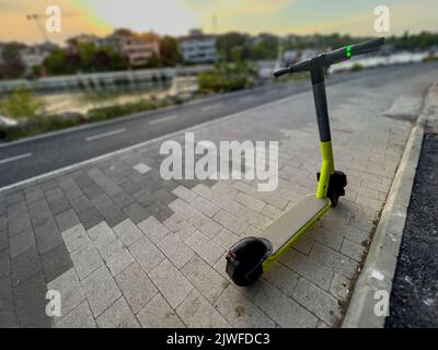 Moderno scooter elettrico 'a noleggio' parcheggiato nella pista ciclabile nelle giornate di sole. Trasporto abbandonato. Quota di trasporto sostenibile dal punto di vista ecologico Foto Stock