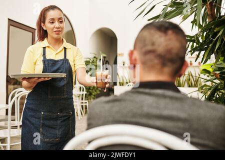 Cameriera sorridente del caffè che porta il caffè ghiacciato al cliente Foto Stock