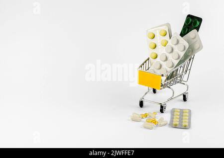 Confezioni con pillole di diversi tipi in un carrello della spesa su sfondo bianco, spazio copia Foto Stock