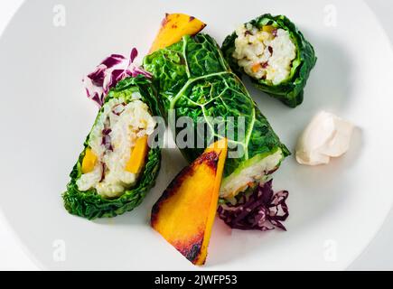 piatto da ristorante vegano: involtini di cavolo savoia con riso e verdure al forno: zucca, ravanello e maionese Foto Stock