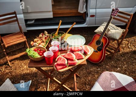 Vista ad alto angolo del tavolo con frutta e insalata al picnic in natura durante il campeggio nella foresta Foto Stock